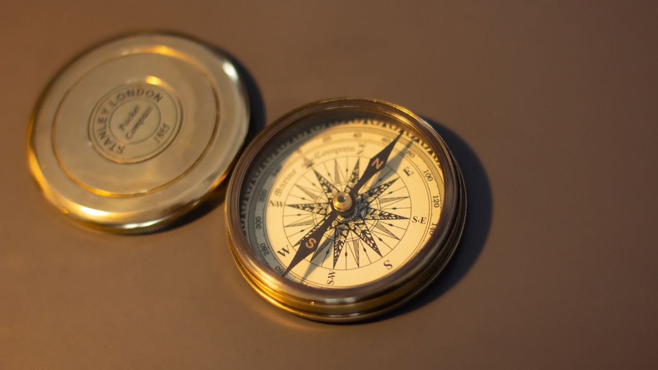 A close-up of a vintage brass compass on a warm brown surface, perfect for exploration themes.