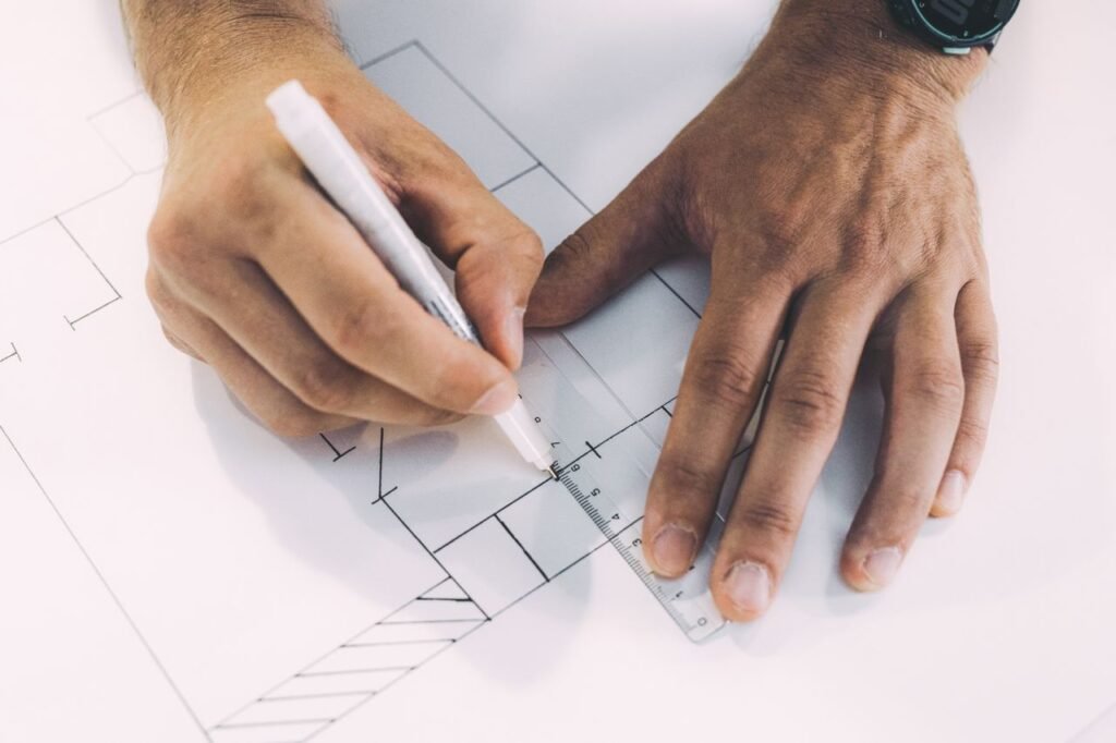 Hands sketching architectural plans with precision using ruler and pen on paper.